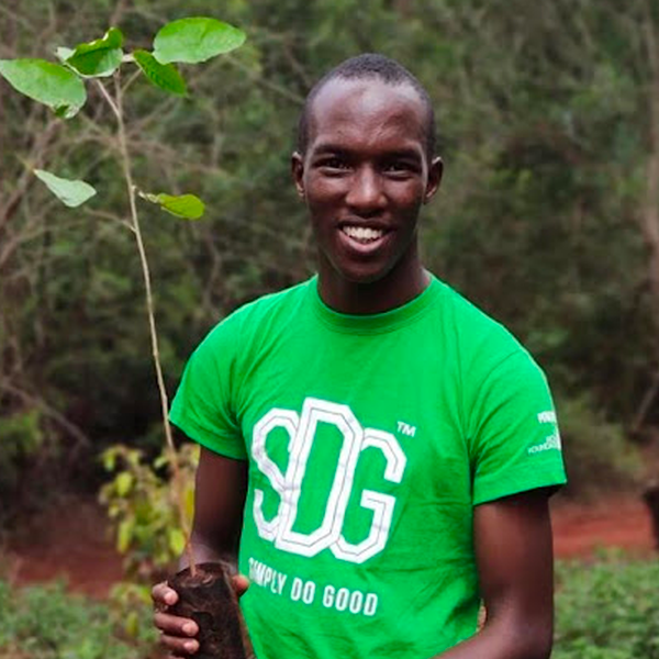 Joseph Nguthiru, a Black man with a deep skin tone, smiles at the camera as he holds a biodegradable package wrapper made from water hyacinth. He is wearing a green shirt that reads, “Simply do good.”