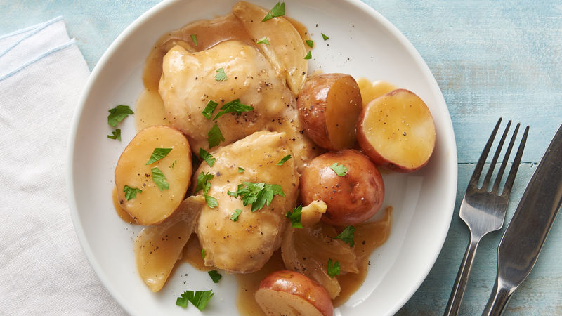 Cooked chicken breasts with halved potatoes topped with sauce, chopped garlic cloves and parsley on a plate.