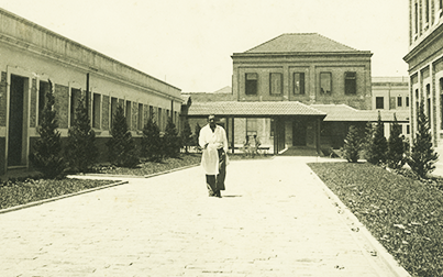 Foto do acervo do Museu mostra os edifícios da enfermaria da antiga Hospedaria de Imigrantes do Brás. Um homem caminha entre os prédios