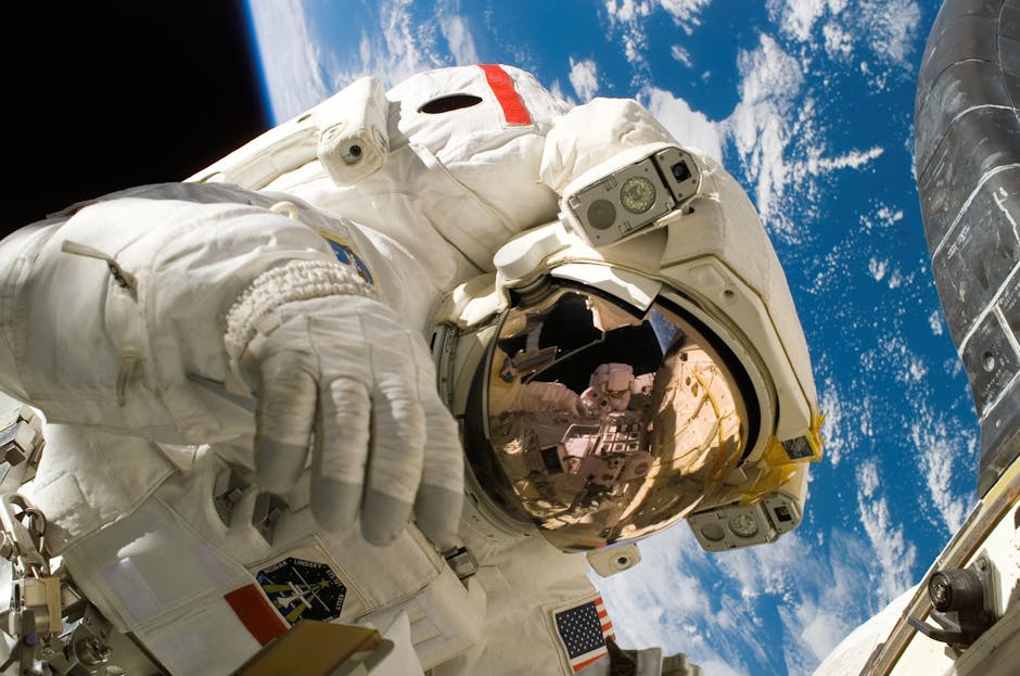 This picture shows an american astronaut in his space and extravehicular activity suite working outside of a spacecraft. In the background parts of a space shuttle are visible. In the far background of the picture planet earth with it's blue color and white clouds is shown as well as a patch of black space.