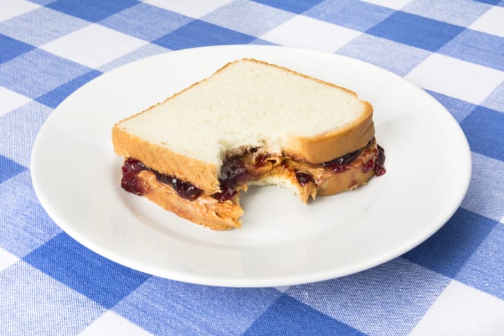 A peanut butter and jelly sandwich on a plate atop a blue and white checked tablecloth