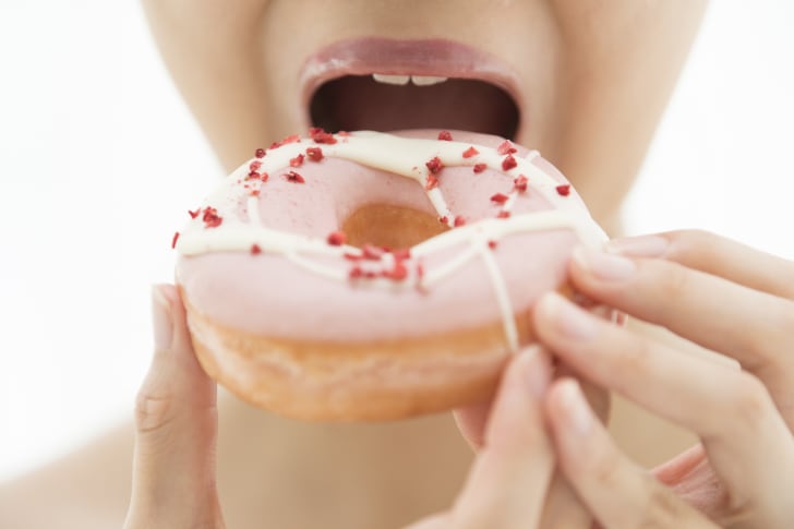 A woman eating a pink frosted donut