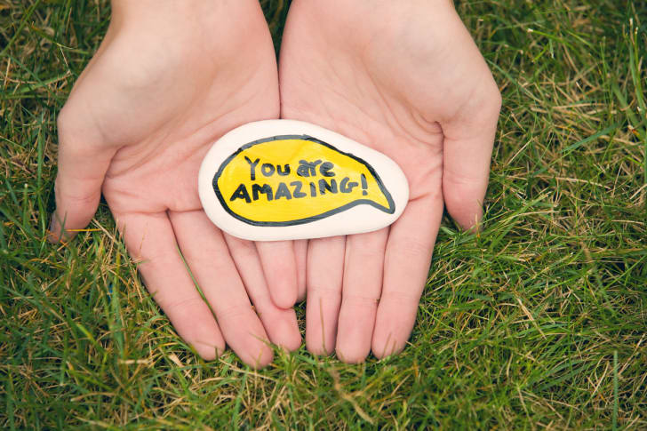 Person holding a rock that says 'You are amazing!' 