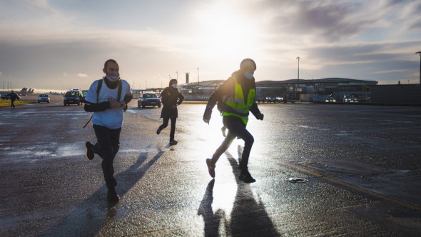 Trois activistes courent sur le tarmac de l'aéroport. Plusieurs véhicules de police sont en arrière-plan.
