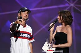 O cantor francês Ken Samaras, também conhecido como Nekfeu (E), ladeado pela apresentadora de TV francesa e mestre de cerimônias Virginie Guilhaume (D), recebe o prêmio de melhor álbum de música urbana durante a 31ª Victoires de la Musique, a cerimônia anual de premiação da música francesa, em 12 de fevereiro de 2016 na sala de concertos Zenith em Paris. AFP PHOTO / BERTRAND GUAY (Foto de BERTRAND GUAY / AFP)