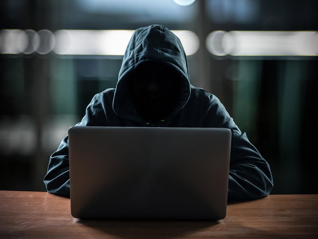 Photo of a hooded person with a hidden face using a computer.