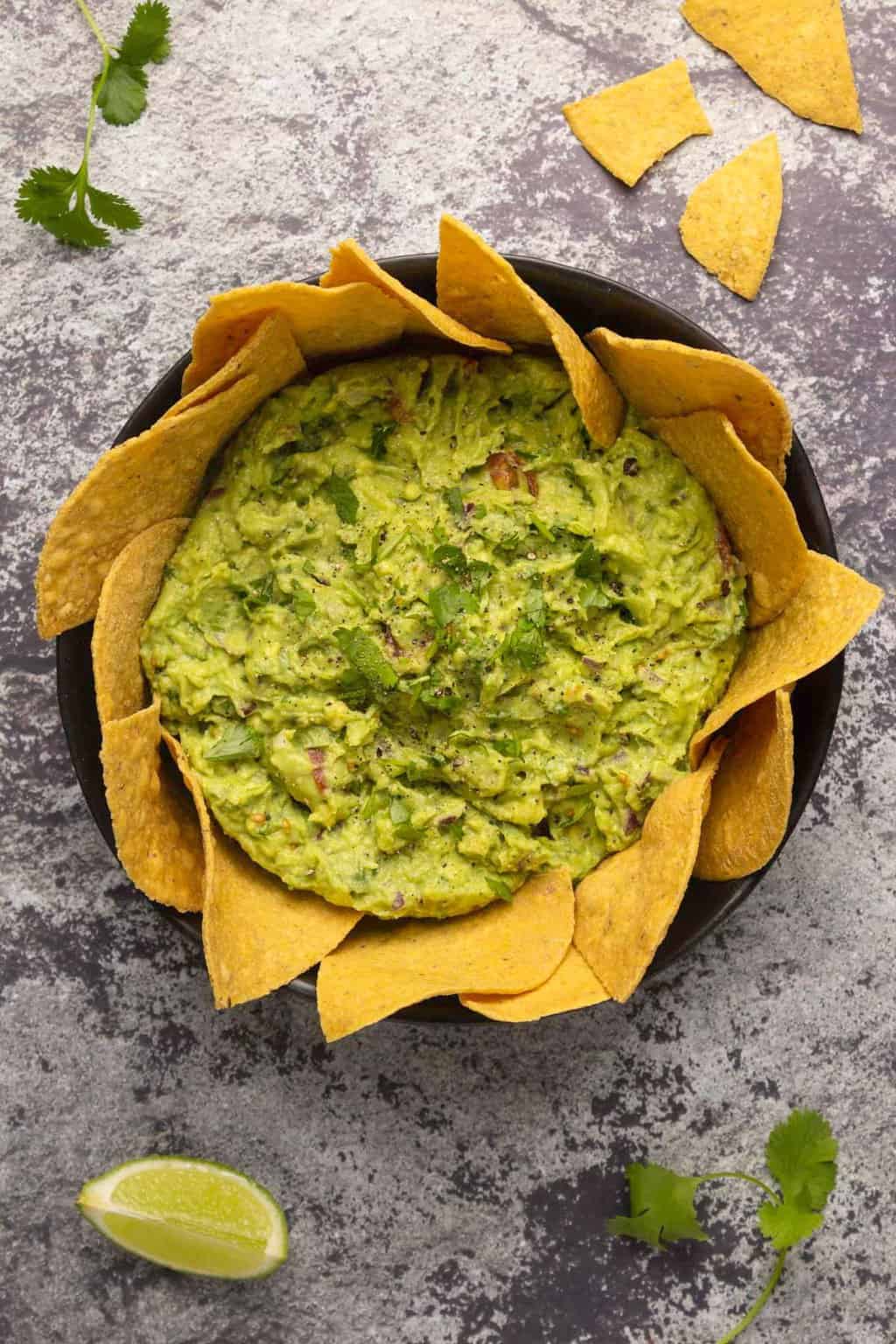 Vegan guacamole surrounded by tortilla chips in a black bowl. 