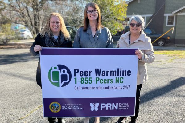 Three people holding up the Peer Warmline sign. 