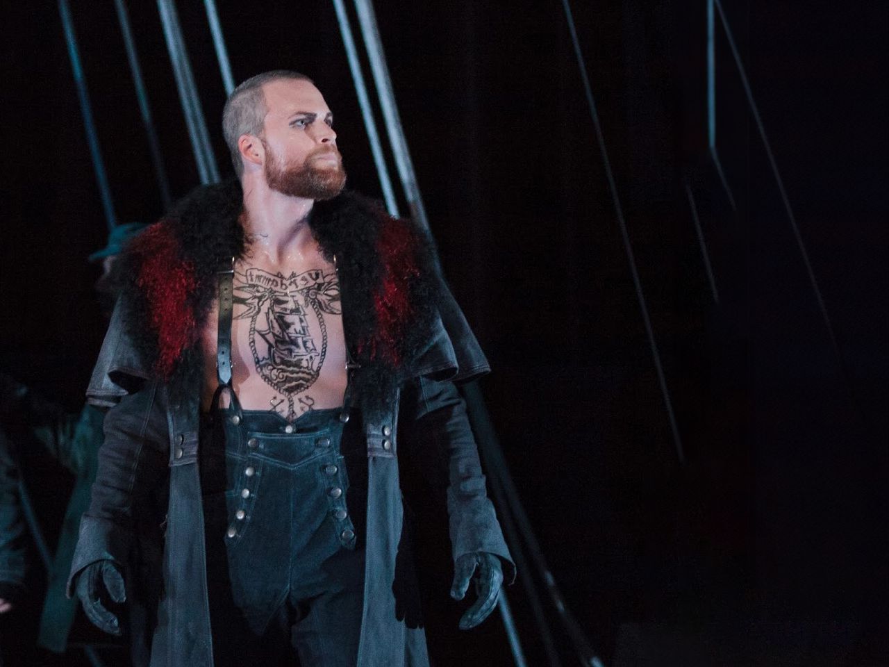 a man with a tattoo on his chest and a coat on a stage
