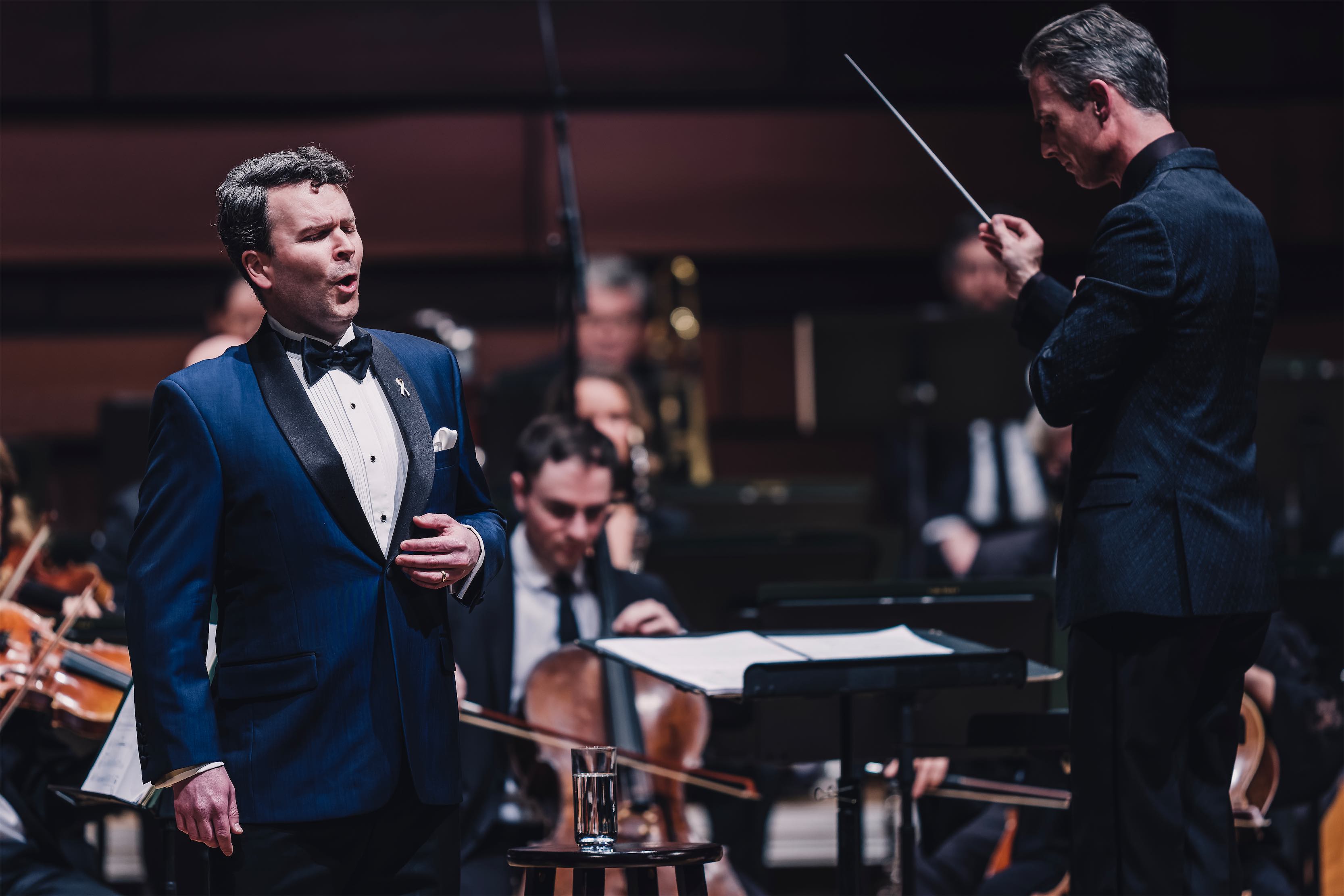 a man in a blue suit and bow tie standing in front of a orchestra