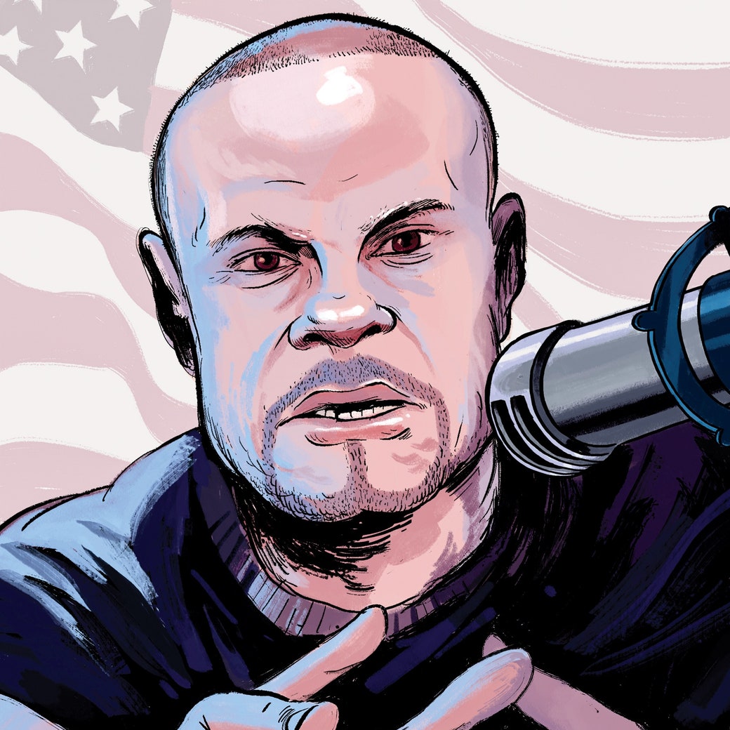 Dan Bongino speaks into a microphone and reaches toward the viewer as he sits in front of a U.S. flag.