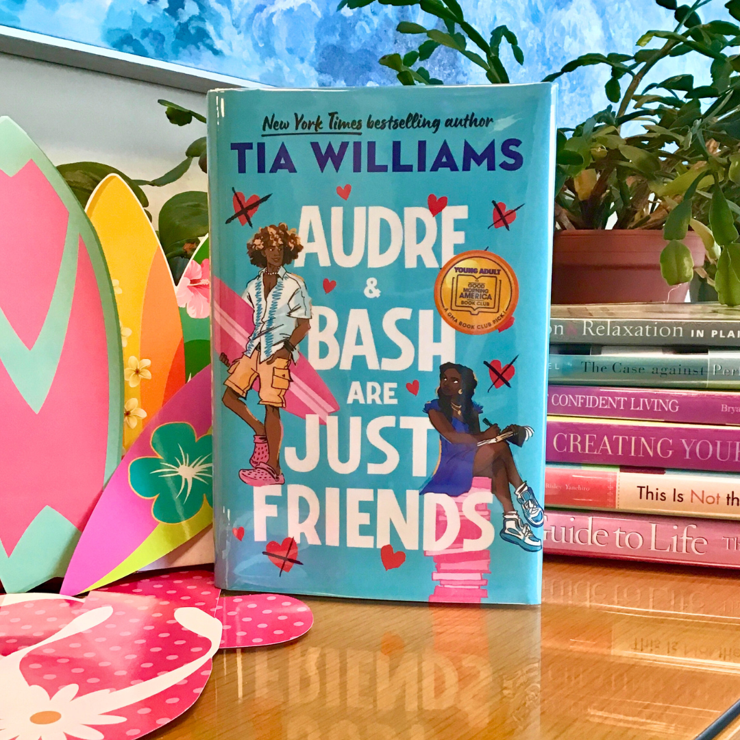 The book shows illustrations of Bash, holding a surfboard and wearing pink crocs, looking back at Audre, writing in a notebook while seated atop a pile of pink books. Around them are many hovering hearts, some of them crossed out with black Xes. The book has been pictured with some cutouts of surfboards and pink sandals on one side, and a stack of self-help books with pink or blue spines on the other to match the cover. The book shows illustrations of Bash, holding a surfboard and wearing pink crocs, looking back at Audre, writing in a notebook while seated atop a pile of pink books. Around them are many hovering hearts, some of them crossed out with black Xes. The book has been pictured with some cutouts of surfboards and pink sandals on one side, and a stack of self-help books with pink or blue spines on the other to match the cover.