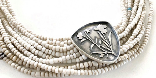 A beaded necklace with a large silver piece at the center with flowers on it