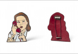 The front and back of a pin designed to look like a woman on the phone