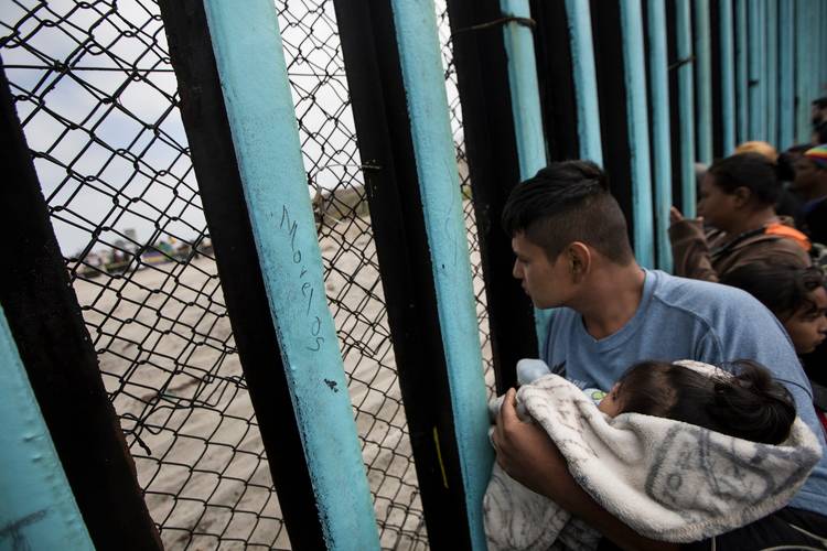 A member of the Central American migrant caravan, holding a child, looks through the border wall April 29 toward a group of people gathered on the U.S. side, as he stands on the beach where the border wall ends in the ocean in Tijuana. (Hans-Maximo Musielik/AP)