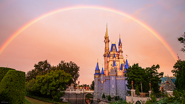 A perfect rainbow arcs high in the sky over Cinderella Castle at dusk.