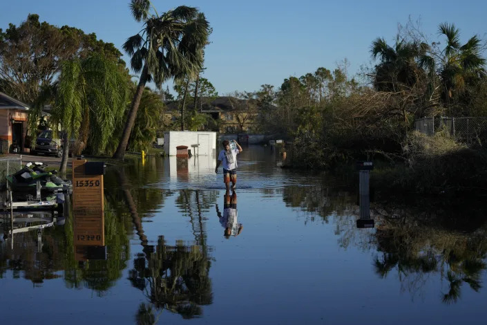 Tony Rivera carries items recovered from his family's waterlogged car through receding flood waters still filling a street in the Harlem Heights neighborhood, three days after the passage of Hurricane Ian, in Fort Myers, Fla., Saturday, Oct. 1, 2022. (AP Photo/Rebecca Blackwell)