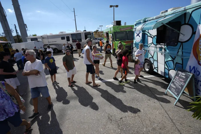 People line up to receive a hot meal from popular Miami food trucks brought in by the non-profit World Central Kitchen, which funds locally-sourced hot meals for people in disaster zones, in Cape Coral, Fla., Saturday, Oct. 1, 2022, three days after the passage of Hurricane Ian. (AP Photo/Rebecca Blackwell)