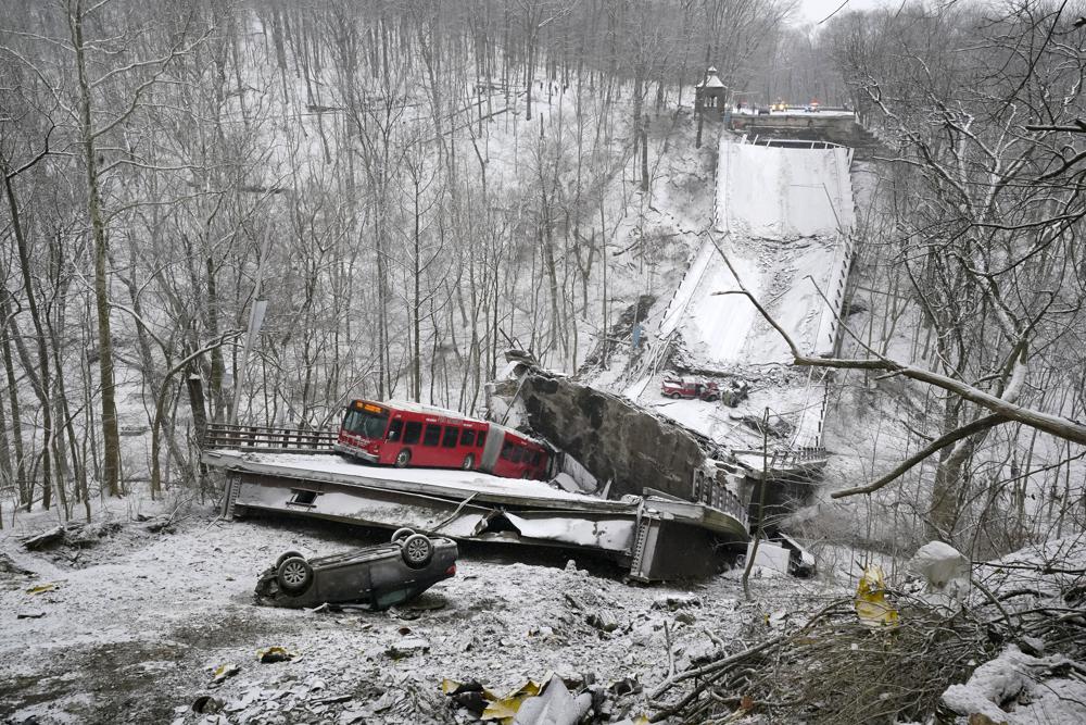 Image of a collapsed bridge over a snowy ditch. There are some overturned cars and also a red city bus on the collapsed road