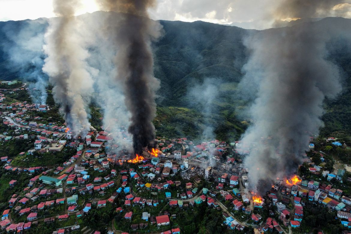 Vue aérienne du village de Thantlang, au Myanmar, où l'on voit la fumée s'élever des incendies des maisons détruites par les tirs d'artillerie des troupes militaires de la junte. Les maisons sont situées sur une montagne couverte d'arbres et de verdure.
