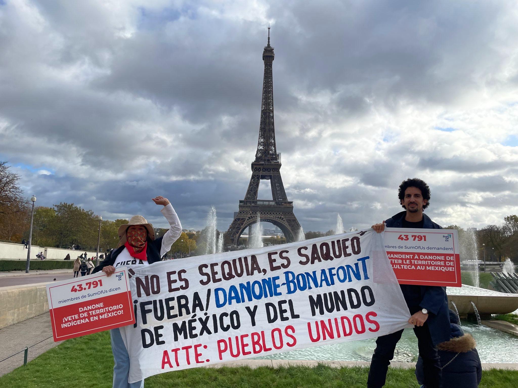 Photo de membres de Pueblos Unidos et SumOfUs avec la Tour Eiffel en arrière-plan. Ils brandissent une banderole et des placards demandant à Danone de quitter la région de Cholulteca au Mexique.