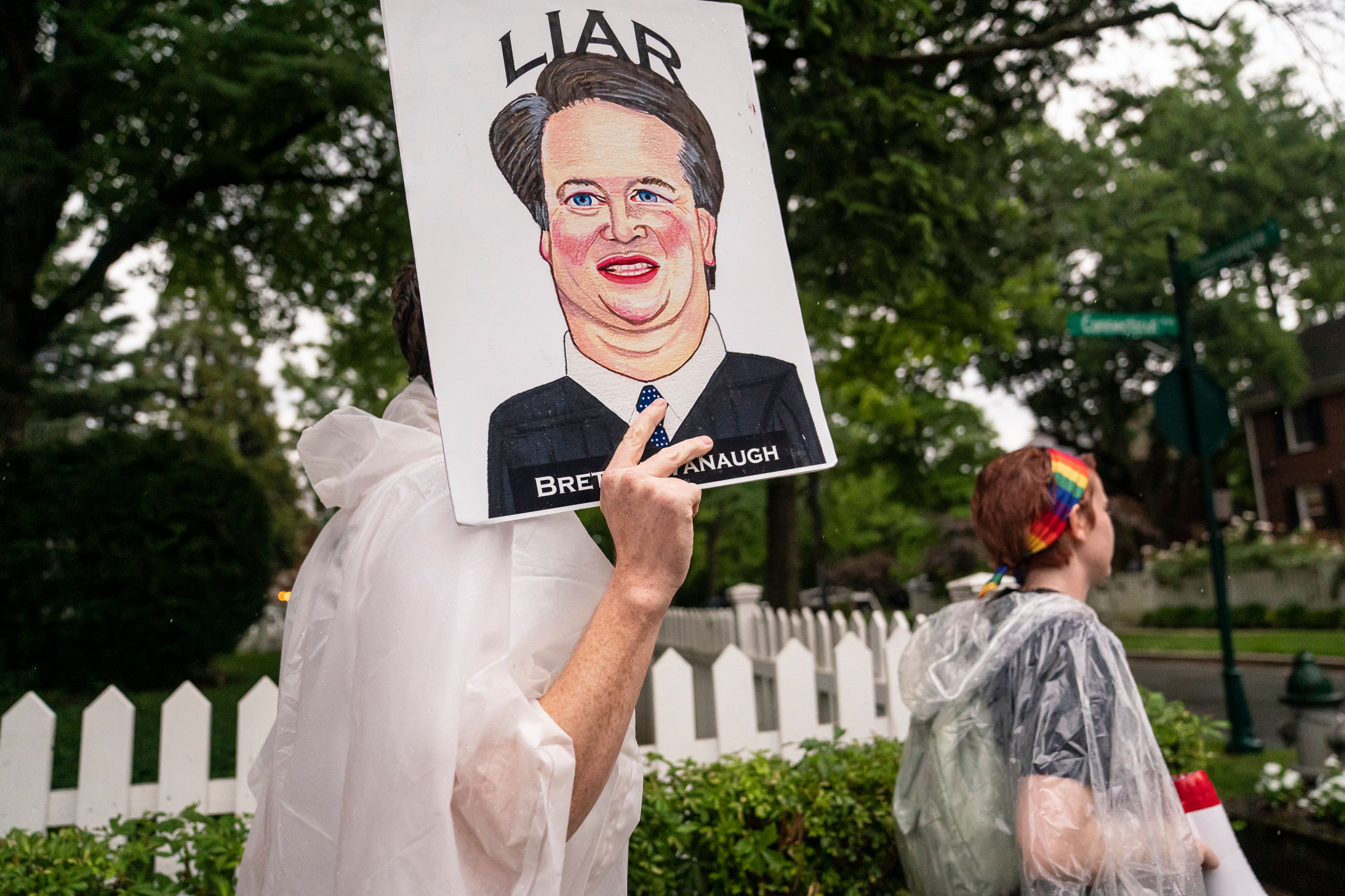Someone holds a poster reading 'Liar - Brett Kavanaugh'