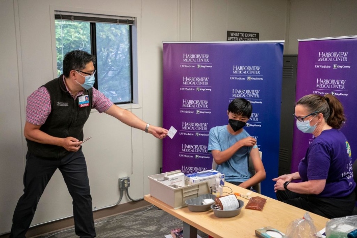 Nightly 8-13-21 photo John Choe hands a vaccine card to his son, Benjamin, after he received a first dose of the Pfizer Covid-19 vaccine from nurse Maureen Stevens at Harborview Medical Center in Seattle.