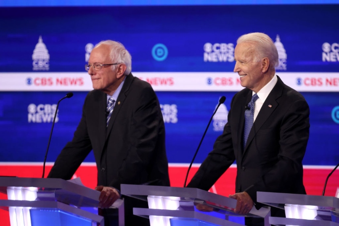 Nightly 10-28-21 photo Democratic presidential candidate Joe Biden smiles as Sen. Bernie Sanders (I-Vt.) (L) looks on during the Democratic presidential primary debate at the Charleston Gaillard Center in February 2020 in Charleston, S.C.