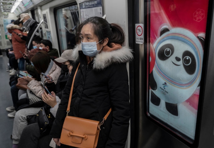 Nightly 1-13-22 photo 3 A woman wears a protective mask as she rides on a metro car next to a logo for Beijing 2022 Winter Olympics mascot Bing Dwen Dwen during rush hour in Beijing.