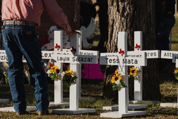 A man places his hand on a cross bearing the names of the victims of a mass shooting in front of Robb Elementary School in Uvalde, Texas.