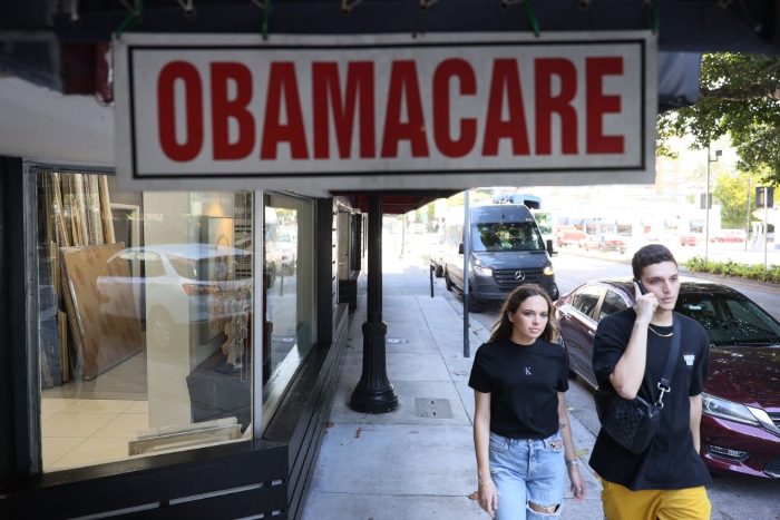 Nightly 11-24-21 photo Pedestrians walk past the Leading Insurance Agency, which offers plans under the Affordable Care Act, in Miami.