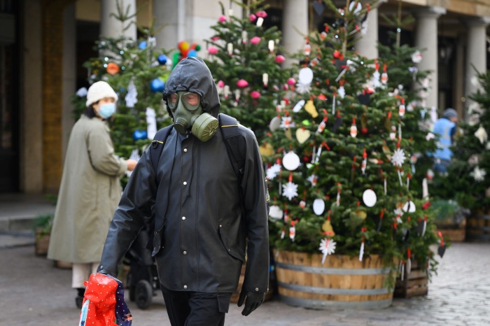 A man wearing full protective clothing and a gasmask walks through the decorated piazza of Covent Garden in London.