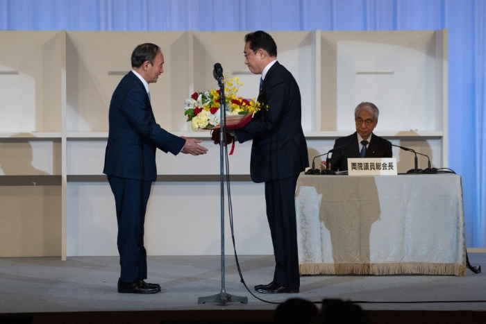 Nightly 9-29-21 photo 3 Japanese outgoing Prime Minister Yoshihide Suga (L) receives a bouquet of flowers from former Foreign Minister Fumio Kishida, after Kishida was announced the winner of the Liberal Democrat Party leadership election in Tokyo.