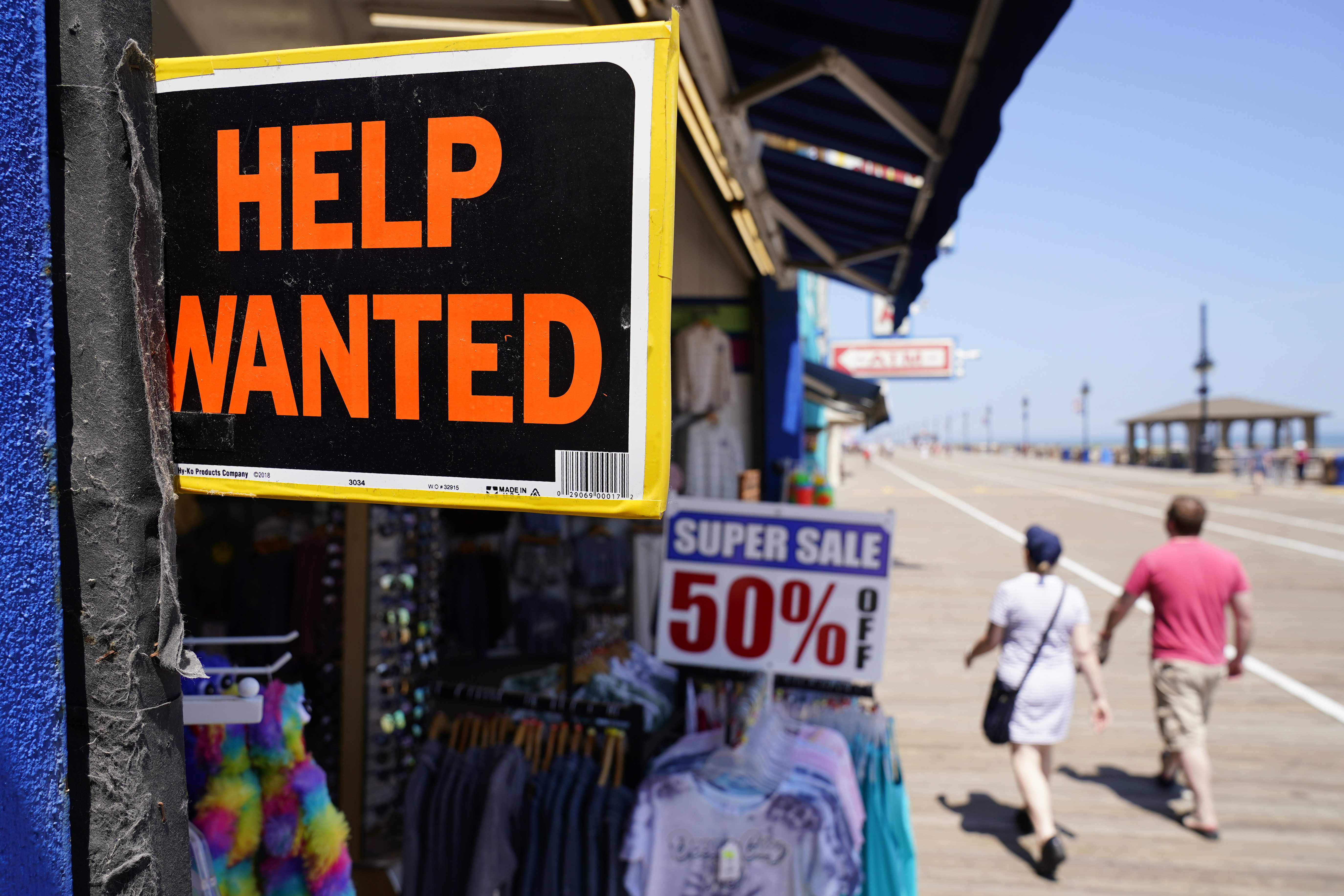 People walk past a help wanted sign in front of a souvenir shop along the boardwalk.