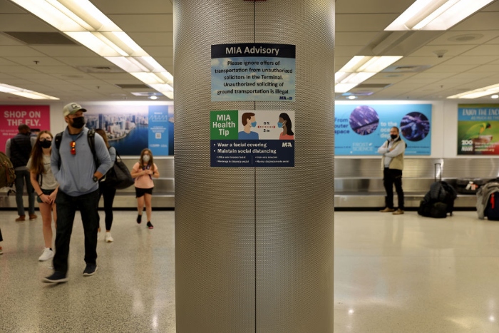 A sign advises people to wear a mask and stand 6 feet apart as travelers make their way through Miami International Airport.