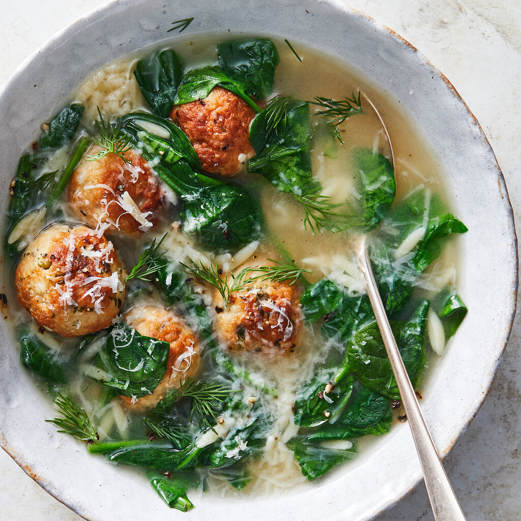 A top-down view of a soup with green leaves and turkey meatballs.