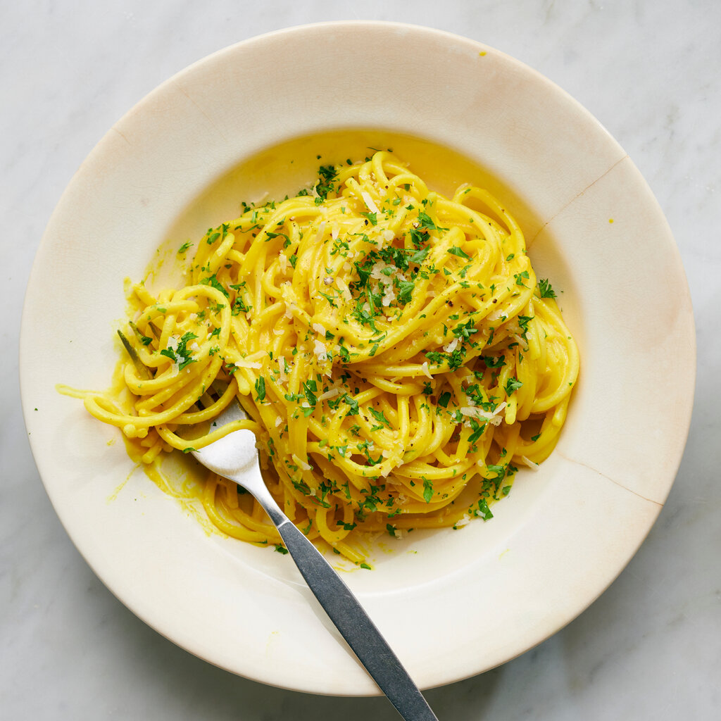 A bowl of yellow-tinted spaghetti with flecks of parsley and Parmesan cheese on top. 