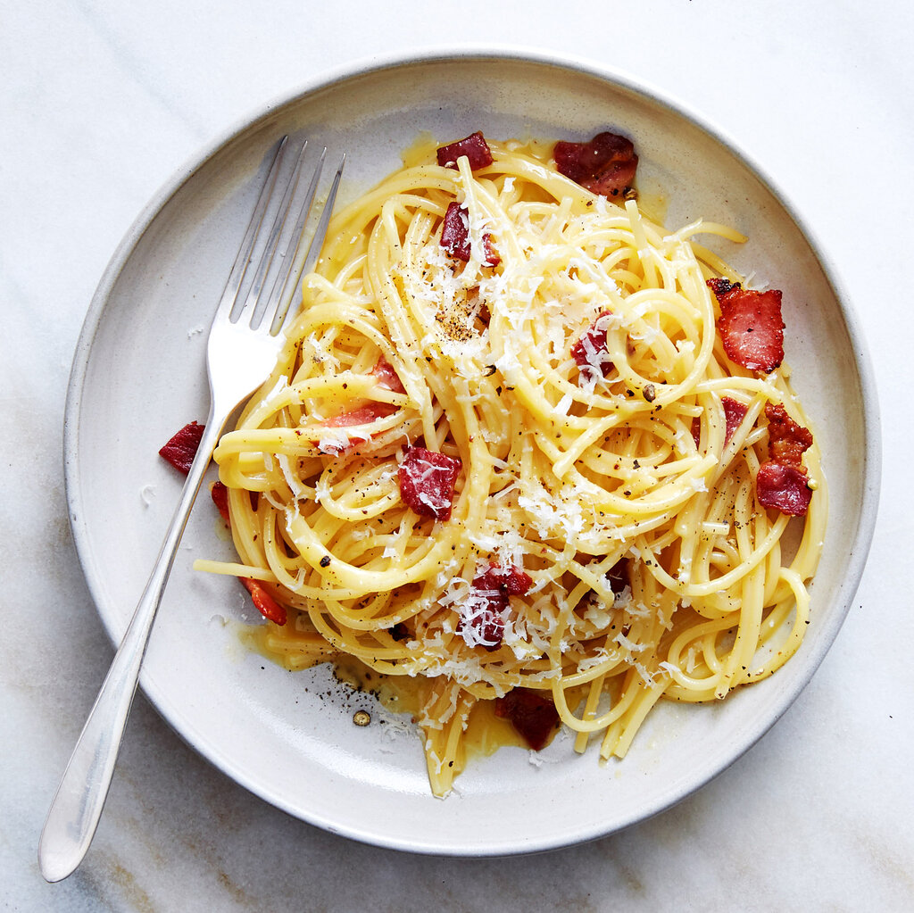 A bowl of spaghetti carbonara on a white plate with a fork.