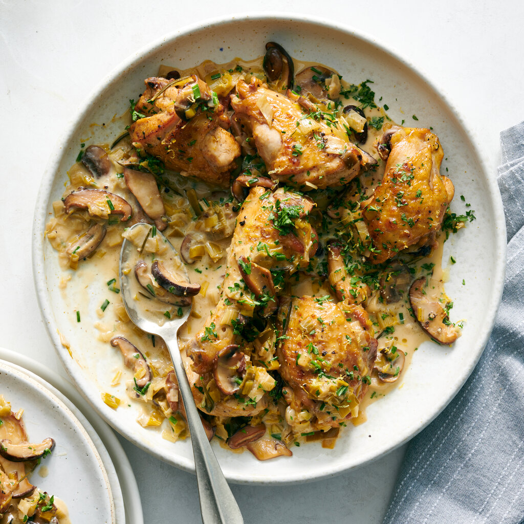 A plate of chicken drumsticks and thighs with mushrooms in a creamy sauce, topped with parsley. 