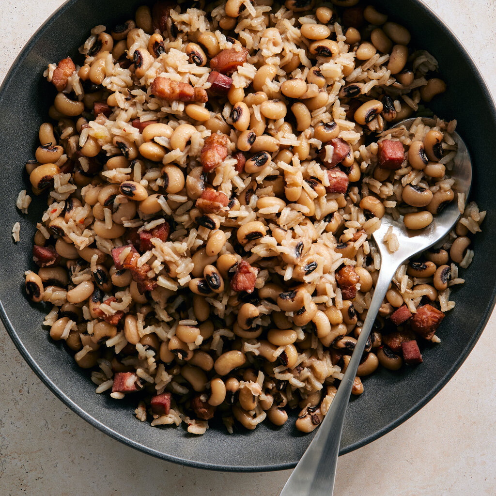 Hoppin’ John, a dish of beans and rice, is shown in a dark gray bowl with a spoon for serving.