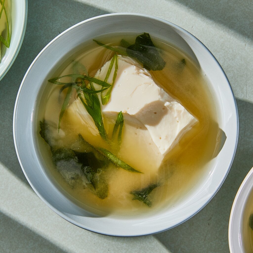 Top down view of a bowl of miso soup with tofu and green onions.