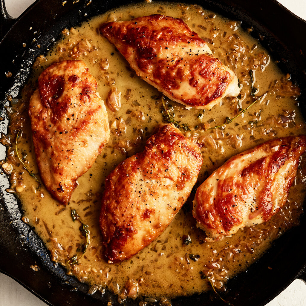Four bronzed chicken breasts sit in a cast-iron skillet filled with an herb-flecked sauce.