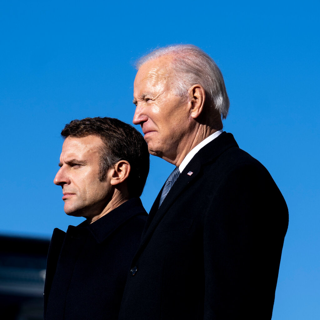 Emmanuel Macron and President Biden standing together under a blue sky.