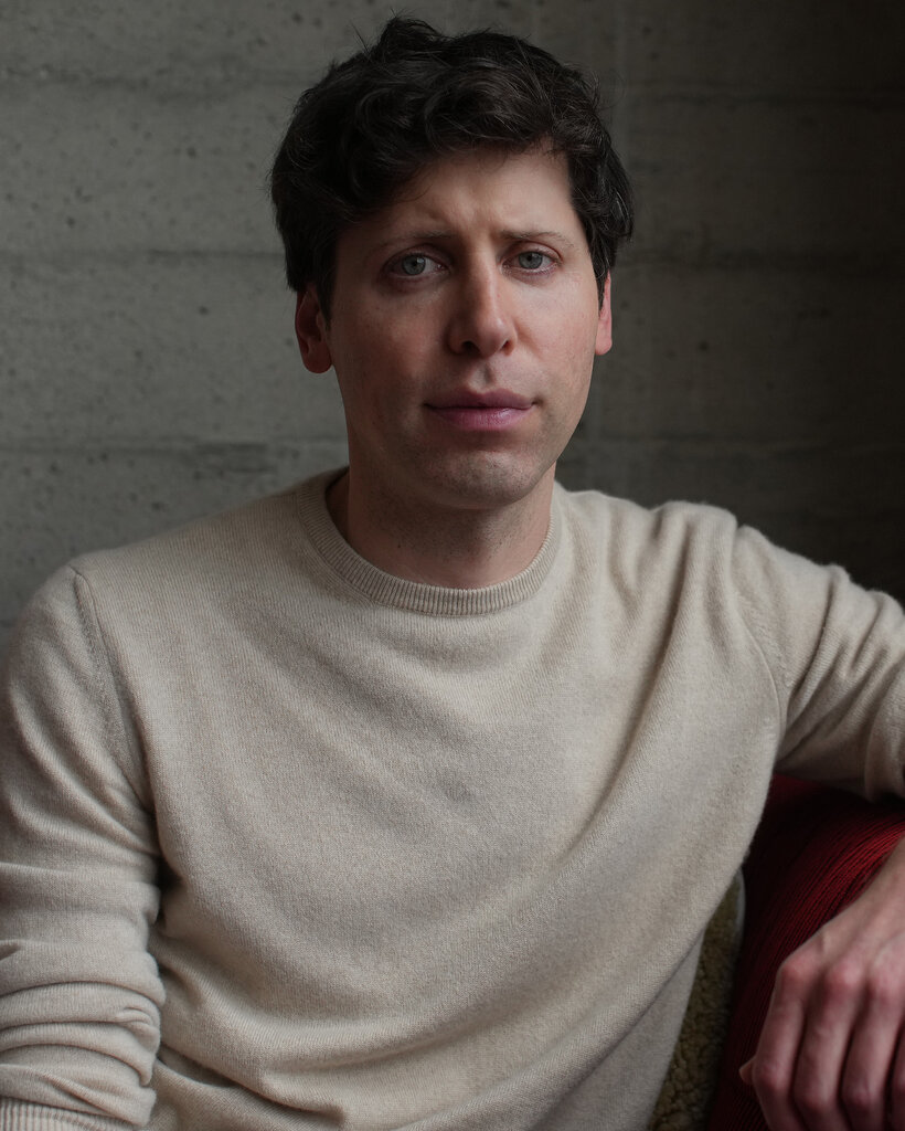 The head and shoulders of Sam Altman, wearing a beige crew-neck sweater and looking at the camera. 