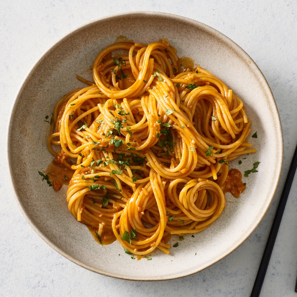 Swirls of spaghetti are coated in a brick-red, buttery gochujang sauce and sprinkled with sliced scallions.