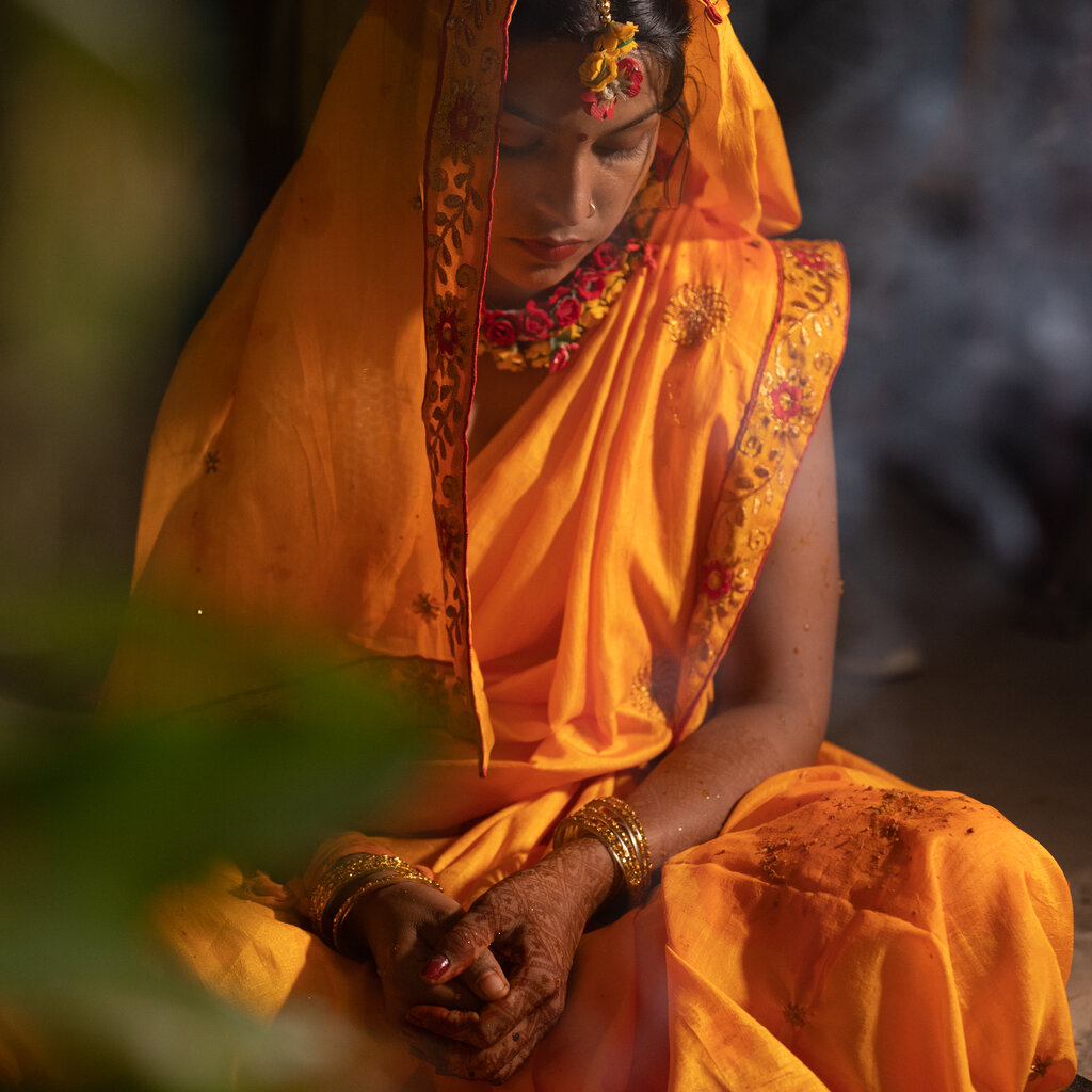 A woman enveloped in orange Indian attire, with henna on her hands, sits in quiet repose.