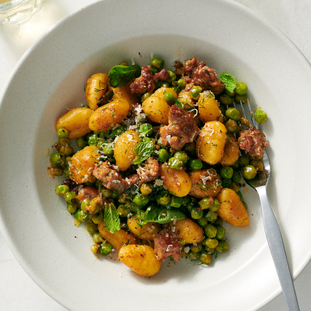 A plate a gnocchi, pieces of sausage and peas. 