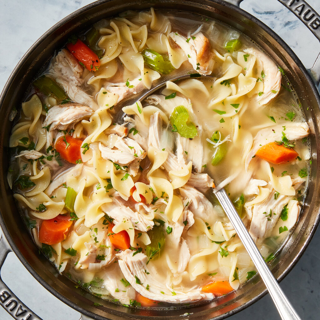 A Dutch oven full of chicken noodle soup with a ladle stuck in for serving.