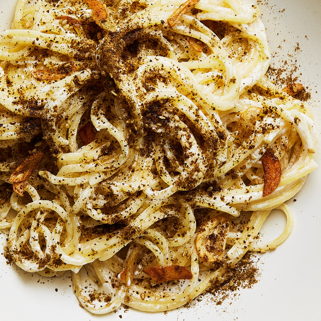 A white bowl holds za’atar and labneh spaghetti on a gray stone table.