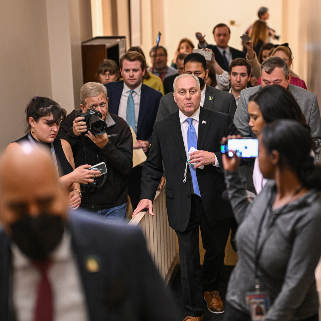 Steve Scalise walks down a hallway in a suit flanked by reporters. 